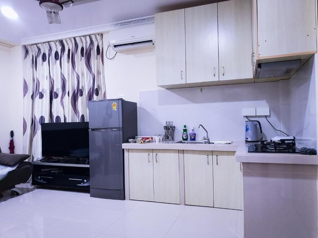 A compact kitchen with a refrigerator, sink, and stove. There is a flat-screen TV and a dining area with a chair.