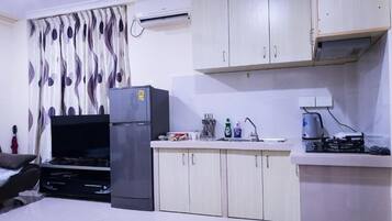 A compact kitchen with a refrigerator, sink, and stove. There is a flat-screen TV and a dining area with a chair.