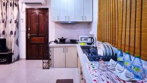 Una cucina con mobili bianchi, una porta in legno, un fornello, un forno a microonde e una finestra con persiane.