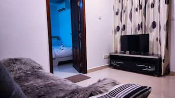 A room with a fur-covered sofa, a television on a black stand, and a patterned curtain.