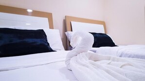 Una camera d'albergo con due letti, biancheria da letto bianca e cuscini scuri.