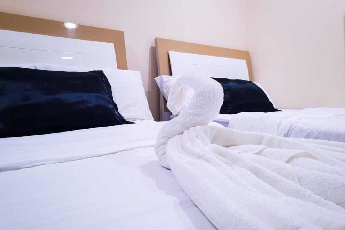 A hotel room with two beds, white bedding, and dark pillows.