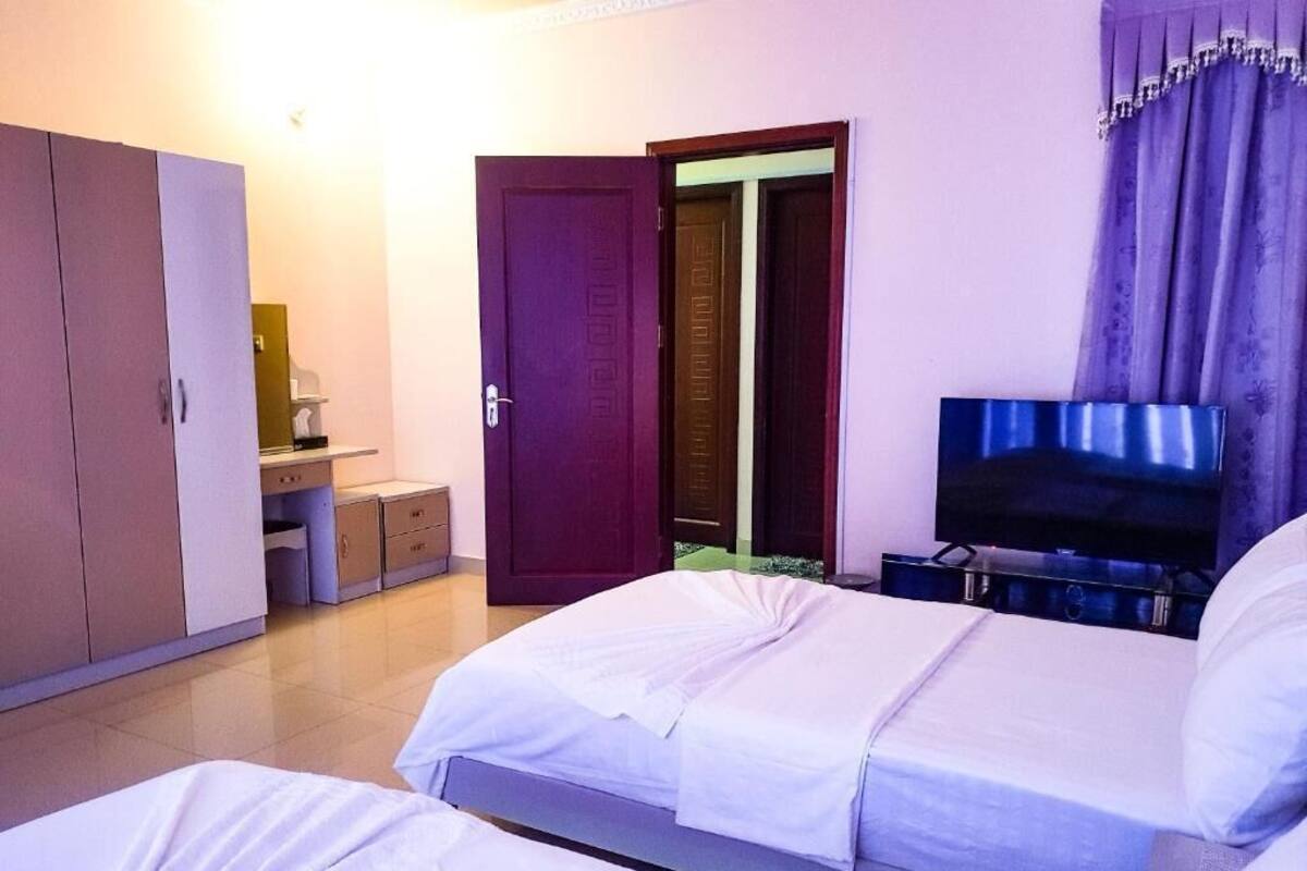 A hotel room with two beds, a wardrobe, a TV, and a door leading to another room.