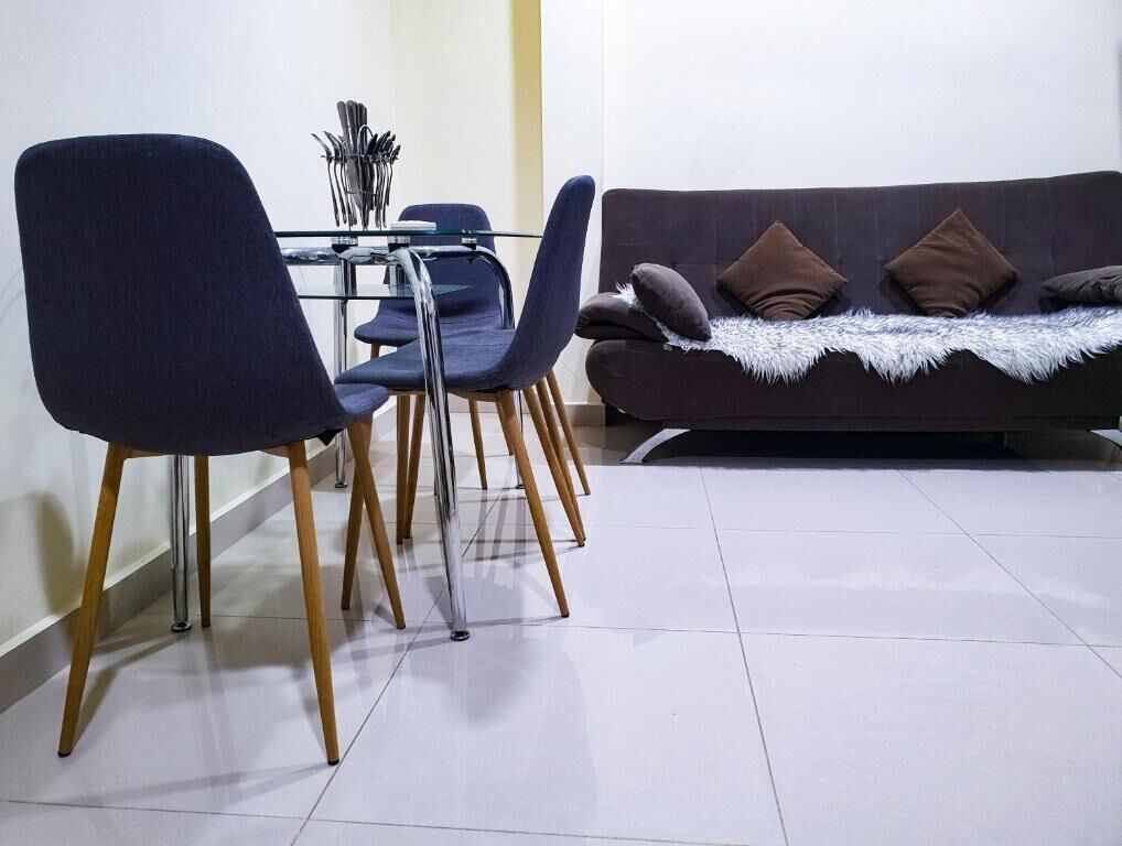 A dining area with a glass table, chairs, and a sofa with cushions.