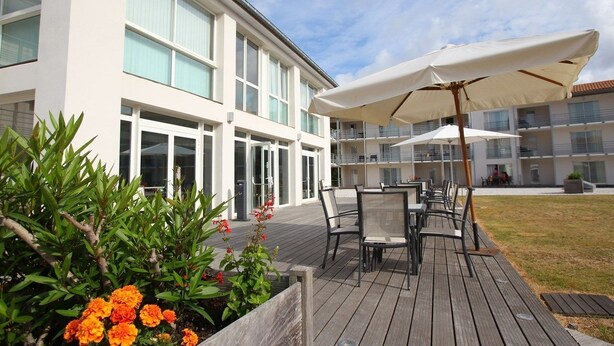 A modern hotel with a wooden deck, outdoor seating, and large umbrellas.