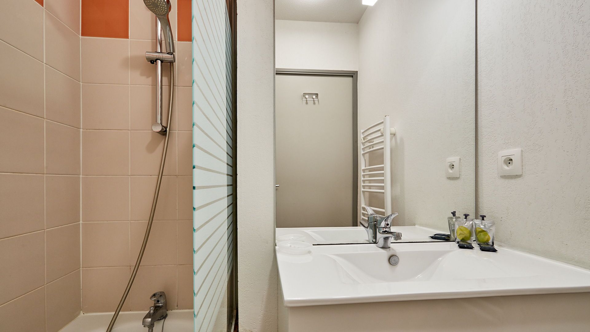 A bathroom with a shower, a sink with a mirror, and toiletries.