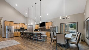 A spacious kitchen with a central island, wooden cabinets, stainless steel appliances, and a dining area with a large window. - Creek View Vacation Home (Rapid City)
