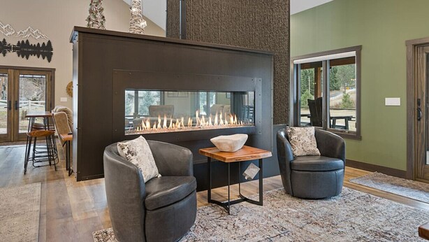 A modern living room with a fireplace, two leather armchairs, a wooden coffee table, and a large window. - Creek View Vacation Home (Rapid City)