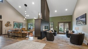 A spacious living room with a fireplace, a dining area with a wooden table and chairs, and a large window offering a view of the outdoors. - Creek View Vacation Home (Rapid City)