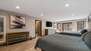 A bedroom with two beds, a wooden bench, a dresser, and a TV on the wall. - Creek View Vacation Home (Rapid City)