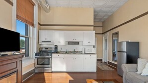 Una cucina moderna con mobili bianchi, un fornello e un forno a microonde. Si nota una TV su un supporto in legno, un divano e un camino.