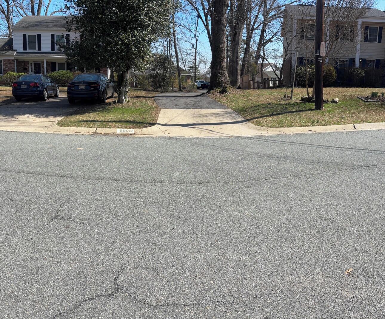 Une rue résidentielle bordée de maisons, avec deux voitures garées, un trottoir et des habitations de chaque côté.