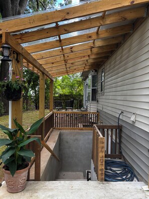 Una terraza de madera con una pérgola, una planta en maceta y una manguera en el suelo.
