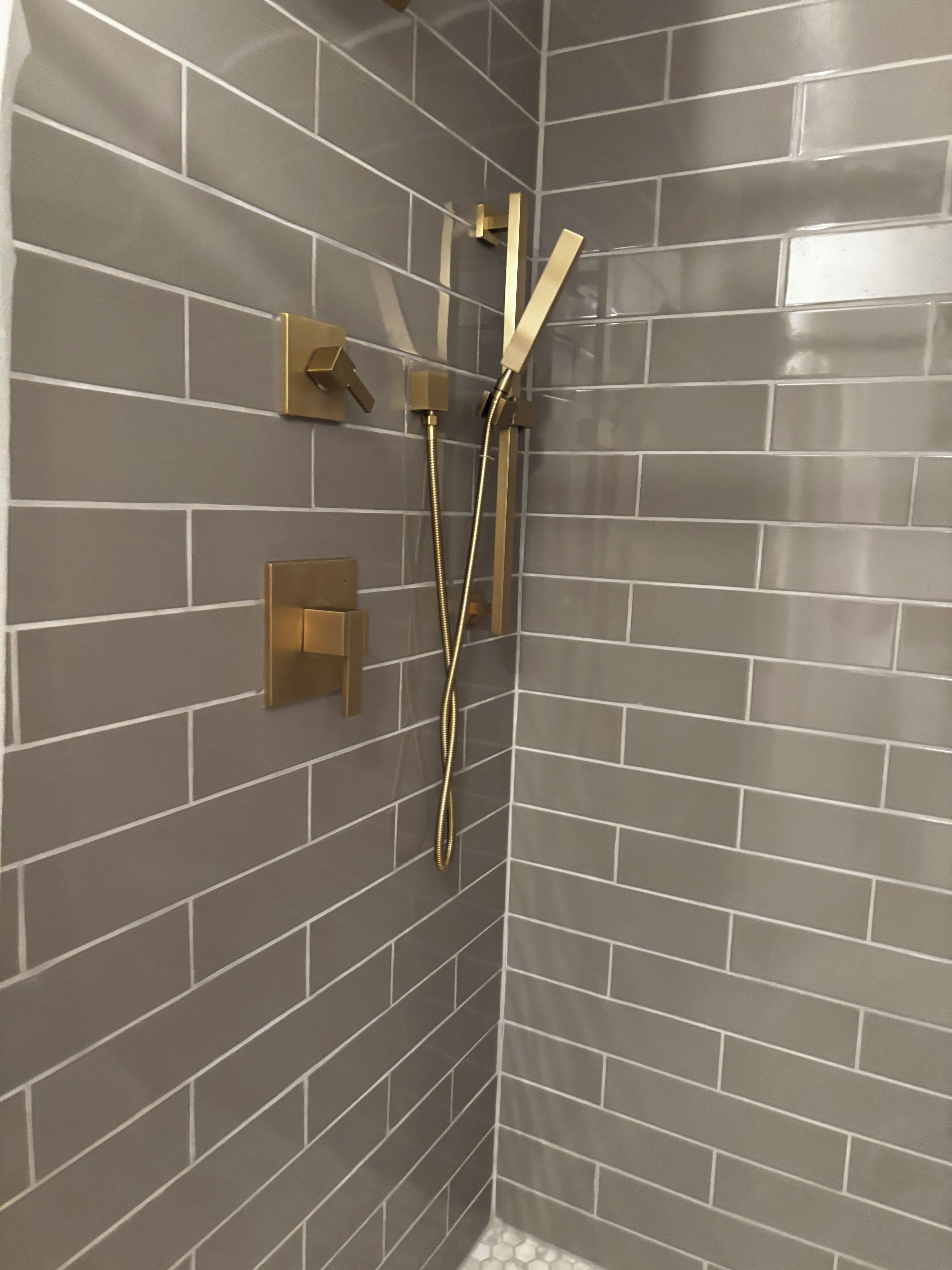 En dusch med modern design, med en kaklad vägg och guldfärgade detaljer.