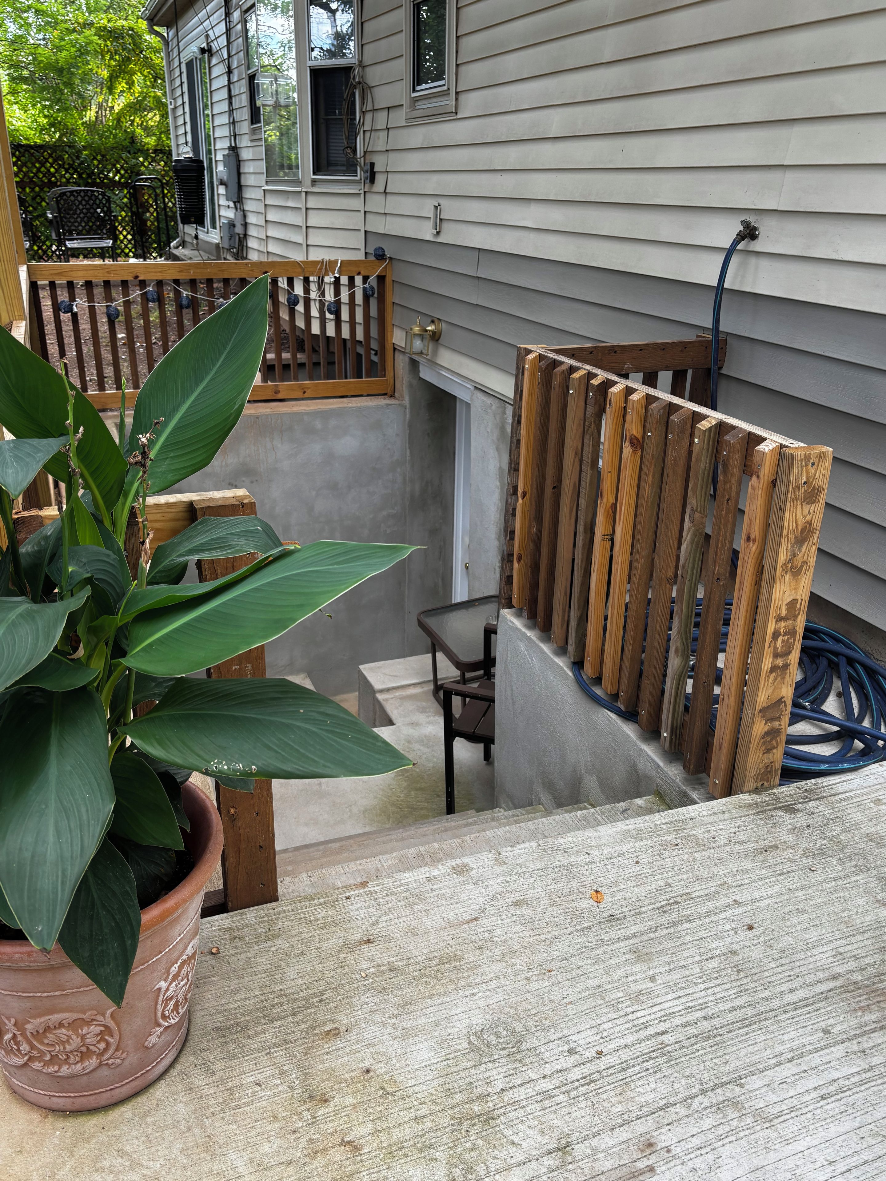 A wooden deck with a potted plant, a metal table, and a wooden fence.