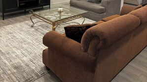A modern living room with a glass coffee table, a sofa, a television, and a bed in the adjacent room. - Delightful 2-bedroom basement apartment in Potomac. (Potomac)