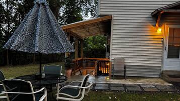 Une terrasse avec des meubles d’extérieur, un parasol à motifs et une maison dotée d’une terrasse en bois.