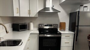 A modern kitchen with white cabinetry, stainless steel appliances, a microwave, oven, and refrigerator. - Delightful 2-bedroom basement apartment in Potomac. (Potomac)