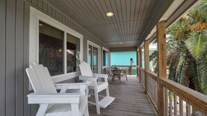A covered porch with white Adirondack chairs, a wooden table, and a view of a turquoise building. - Canal Fishing Retreat - Dock, Sky Deck, Golf Cart (Rockport)