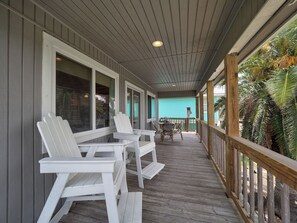 En inglasad veranda med vita Adirondack-stolar, ett träbord och utsikt över en turkosfärgad byggnad.