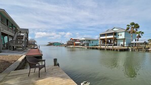 A waterfront property with a wooden dock, a covered seating area, and buildings with balconies and outdoor spaces. - Canal Fishing Retreat - Dock, Sky Deck, Golf Cart (Rockport)