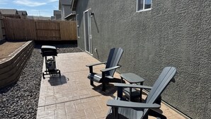 Eine Terrasse mit Adirondack-Stühlen, einem Grill und einem Steinbelag.
