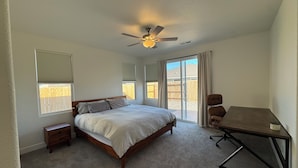Ein Schlafzimmer mit Bett, Schreibtisch, Stuhl, Deckenventilator und einem Fenster mit Jalousien.