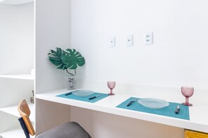 Eine Küche mit weißen Arbeitsflächen, einer blauen Matte, einer Pflanze und pinkfarbenem Glas.