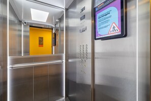 Ein Fahrstuhlinneres mit gelber Tür, Notanweisungen und einem digitalen Display.