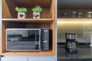 Een keuken met een magnetron, koffiezetapparaat, houten planken met planten en een aanrecht.
