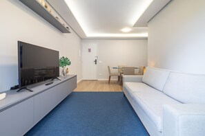 A modern living room with a flat-screen TV, a sofa, a dining table with chairs, and a blue carpet. - Jabaquara 53 2q 4p (São Paulo)