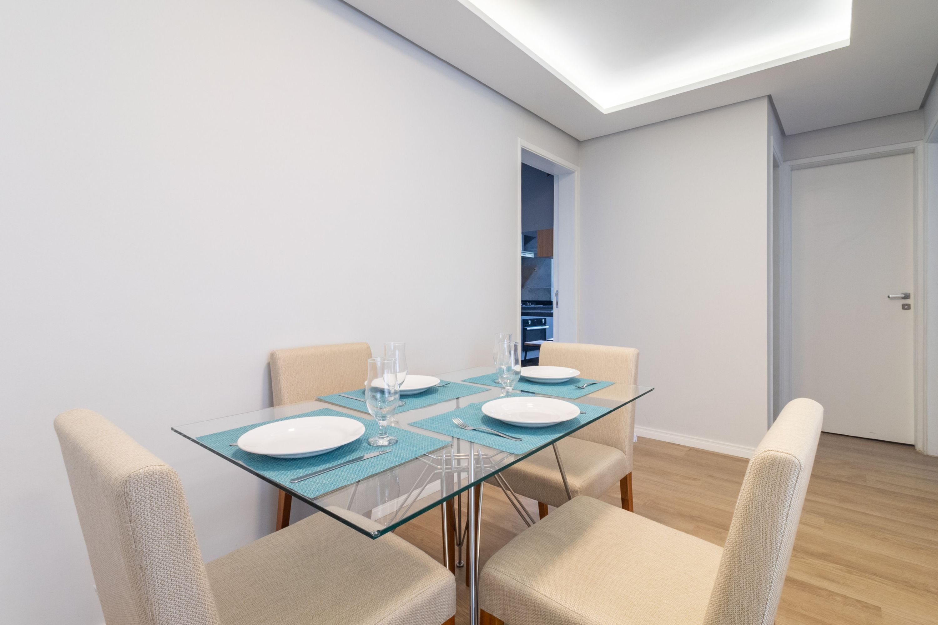 Een moderne eethoek met een glazen tafel, vier stoelen en een plafondlamp.