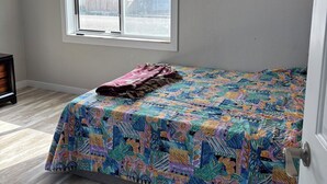 Una camera da letto con un letto, una finestra con persiane, una ventola a soffitto e una porta.