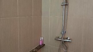 Une douche équipée d’un pommeau de douche à main, d’un robinet mural et d’un panneau de commande.