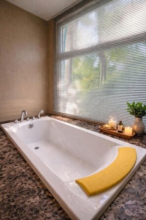 A bathroom with a rectangular bathtub, a window with blinds, a granite countertop, and a small plant on the side. - Seaview Spirit Private Pool Villa (Hua Hin)