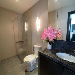 A modern bathroom with a glass shower enclosure, a toilet, a sink with a marble countertop, and a vase of pink flowers. - Seaview Spirit Private Pool Villa (Hua Hin)