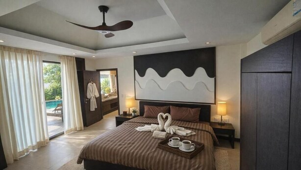 Une chambre d’hôtel moderne dotée d’un grand lit, d’un ventilateur de plafond, d’une vue sur l’extérieur et d’une œuvre d’art accrochée au mur.