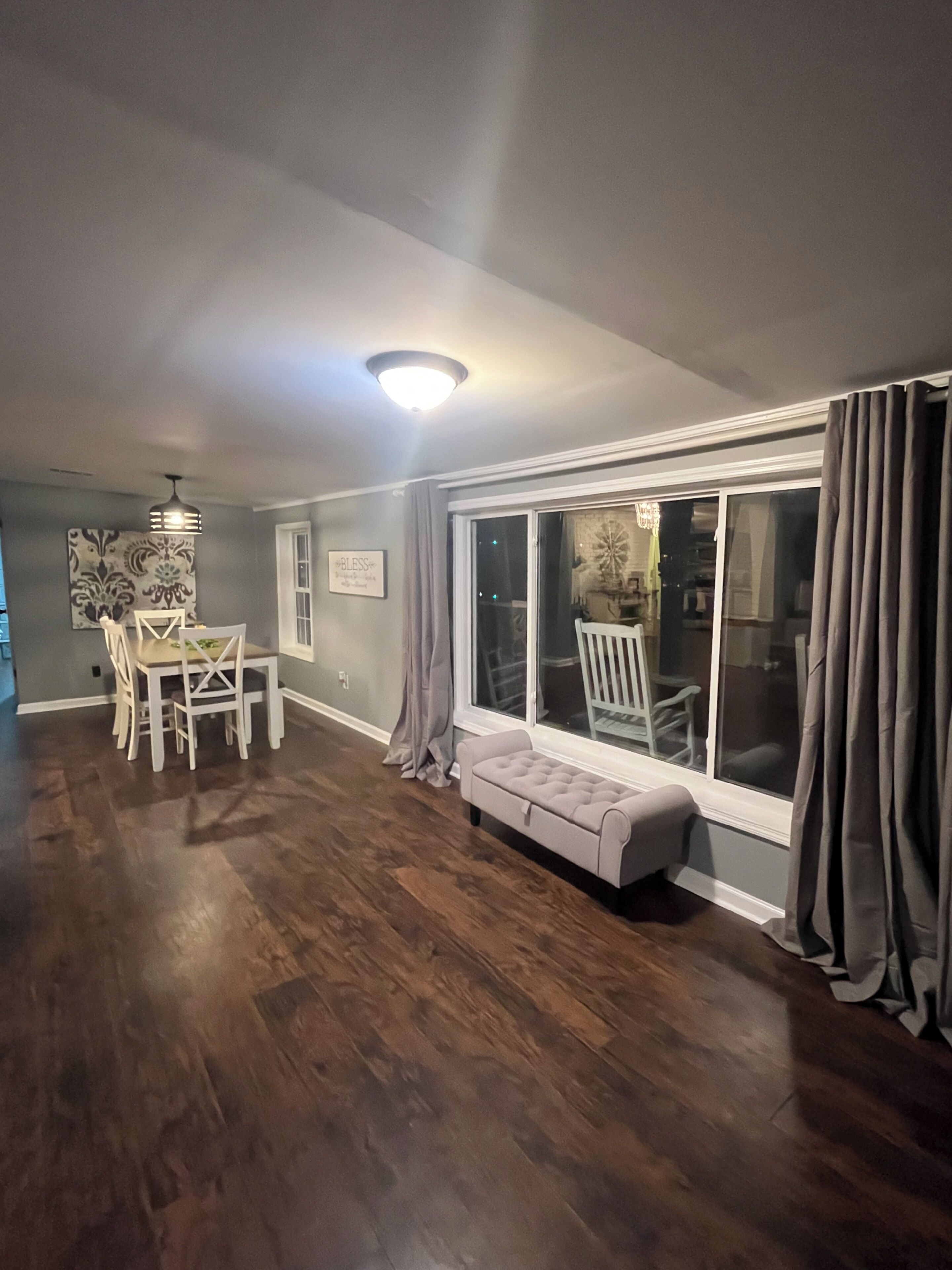 A spacious room with a dining area, a bench by the window, and a ceiling light fixture.