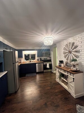 Une cuisine moderne dotée d’un îlot central, d’appareils électroménagers en acier inoxydable, d’un lustre et d’un élément décoratif mural.