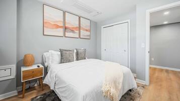 Een slaapkamer met een bed, nachtkastje, lamp en een kunstwerk aan de muur.