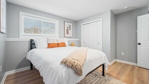 Een slaapkamer met een bed, een raam met jaloezieën, een deur en een vloerkleed.