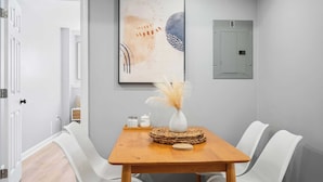 Een modern interieur met een houten tafel, witte stoelen, een vaas met gedroogde bloemen en een kunstwerk aan de muur.