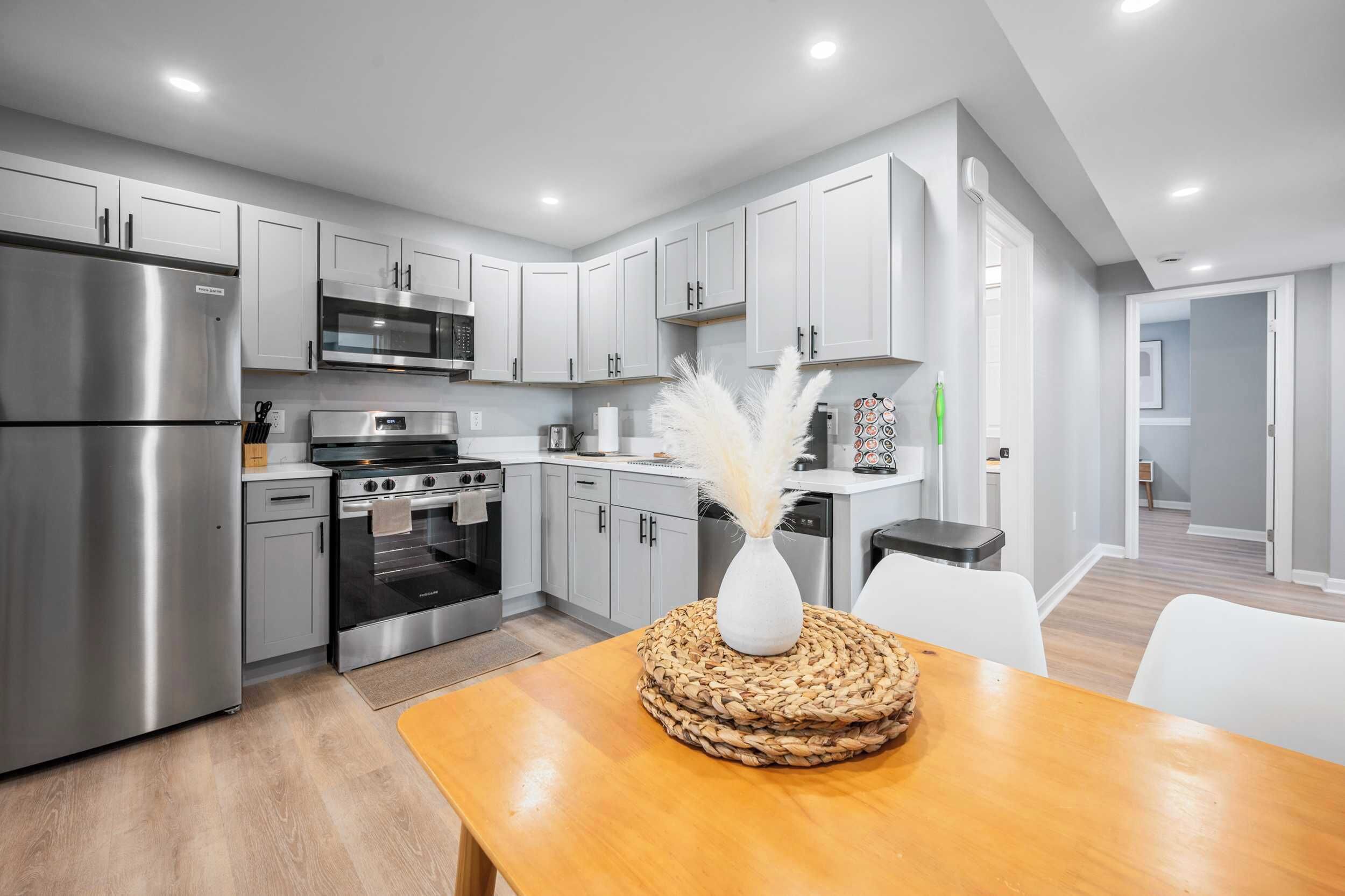 A modern kitchen with stainless steel appliances, grey cabinets, and a wooden dining table with a woven placemat.