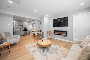 A modern living room with a sofa, a round wooden coffee table, a fireplace, and a TV mounted on the wall. - The Quattro-Lux at Charles 4BR / 2BA with "P"+Ldry PVD. Near Providence College (Providence)