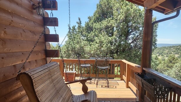 Eine Holzterrasse mit einer Schaukel, einer Bank und Blick auf Bäume und Hügel.