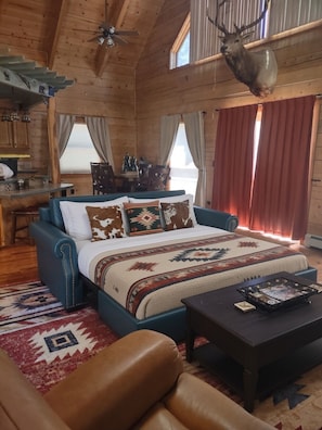 Ein rustikales Blockhaus-Interieur mit einem Bett, einem Couchtisch, einer Couch und einem aufgehängten Hirschkopf.