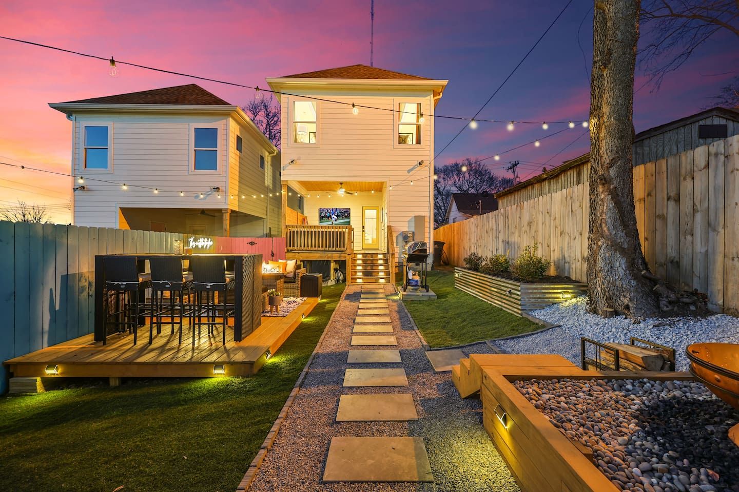 Una casa de dos pisos con un balcón, asientos exteriores y una chimenea al aire libre.
