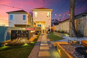 Ein zweistöckiges Haus mit einer Terrasse, Sitzgelegenheiten im Freien und einer Feuerstelle.