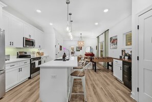 Eine moderne Küche mit weißen Schränken, einer zentralen Kochinsel und einem Essbereich mit Holztisch und Stühlen.