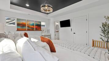 Un dormitorio moderno con una cama grande, una araña, obras de arte en la pared y un televisor.